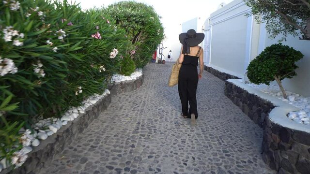Happy lady in black elegant clothes enjoying her holidays on Santorini, Greece walking on coblestone street in Oia
