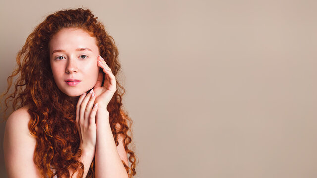 portrait of smiling girl with long curly red hair in the studio on a beige background
