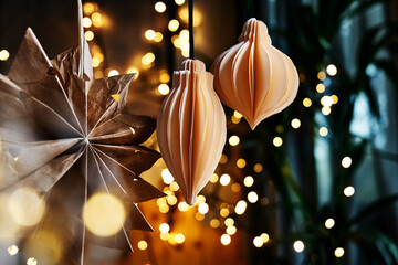 Alternative christmas tree. Handmade paper christmas decorations scandi style on the branch on blurred christmas lights background.Zero waste winter holidays decoration