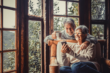 Couple of two old and mature people at home using phone together in sofa. Senior use smartphone...