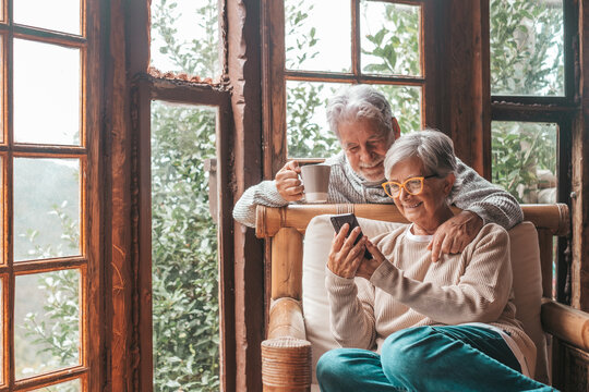 Couple of two old and mature people at home using phone together in sofa. Senior use smartphone having fun and enjoying looking at it. Leisure and free time concept in the living room.