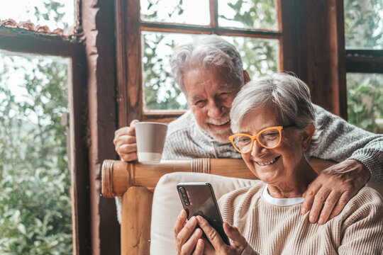 Couple of two old and mature people at home using phone together in sofa. Senior use smartphone having fun and enjoying looking at it. Leisure and free time concept in the living room.