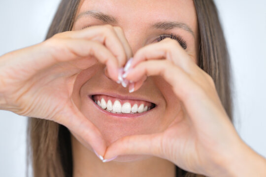 Teeth care. Woman with beautiful smile with strong white teeth. Dental care. Woman holding heart shaped hands near perfect healthy teeth. Stomatology or dentistry concept