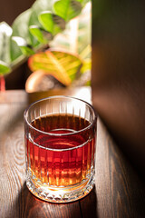 Faceted glass of whiskey on a wooden table against the background of exotic plants.