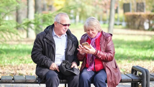 Happy senior couple laughing and exciting with something in smartphone mobile while sitting in the park