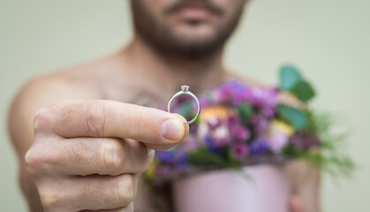 The serious adult shirtless man holds the wedding ring in his hand, proposing to marry.