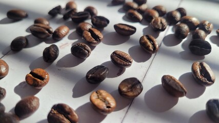 Coffee beans, scattered around on white wood background on sunlight under windows shades shadows, arabica coffee beans, organic Brazilian coffee