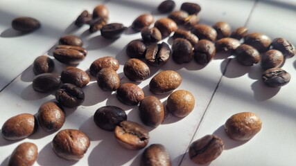 Coffee beans, scattered around on white wood background on sunlight under windows shades shadows, arabica coffee beans, organic Brazilian coffee