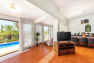 Modern traditional European living room with TV dinner table overlooking the pool and garden with palm trees.