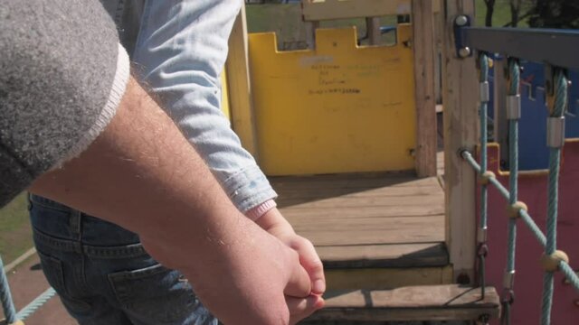 Delighted girl with long plait walks along colourful amusement park attraction holding dad hand. Concept holiday