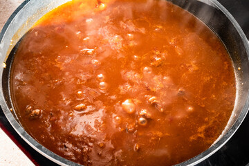 cooking goulash with beef, tomato and paprika in deep frying pan at home kitchen