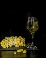 Fresh grapes and a crystal wine glass of white wine on a black background. Stock Image.
