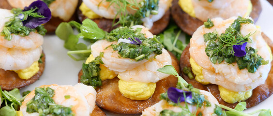 Delicious canapes with prawns, spicy sauce, herbs and edible flowers