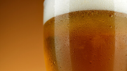 Cold Glass of beer close up with froth. Cold Light Beer in a glass with water drops. Craft Beer close up on brown background