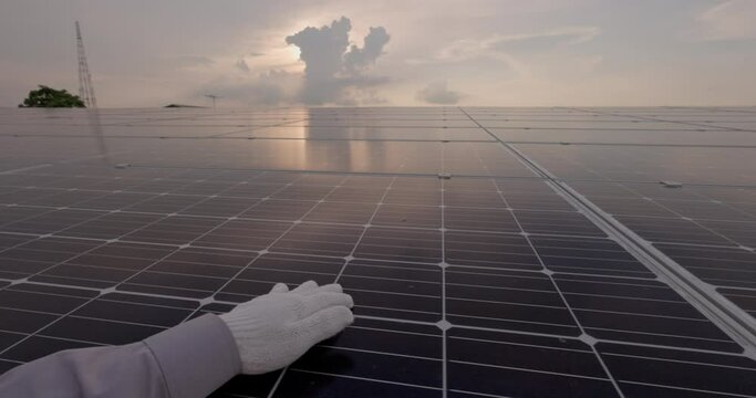 Men's hand strokes the surface of solar panels in close-up. On a sunset, a young engineer hand inspects the operation of the sun and the cleanliness of photovoltaic solar panels.