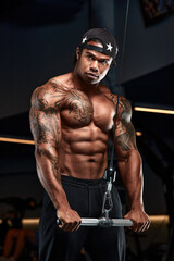 Fototapeta na wymiar Strong and muscular dark skin man trains on modern equipment in gym. Portrait of muscular pumped up fitness trainer