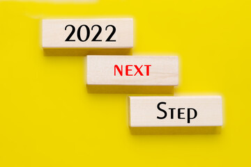2022 next step in text on wooden blocks on yellow background. Business motivation or inspiration,...
