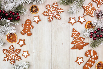 Obraz na płótnie Canvas Christmas frame of gingerbread cookies and frosty tree branches. Top view on a rustic grey wood background with copy space.