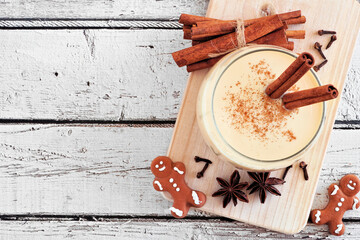 Spiced Christmas eggnog. Above view on a serving board with gingerbread cookies on a white wood...