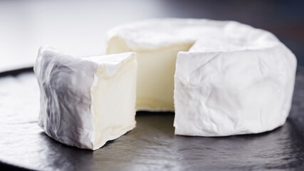 Camembert on a dark background. Soft cheese with white mold on a black plate. Minimalism. Copy space
