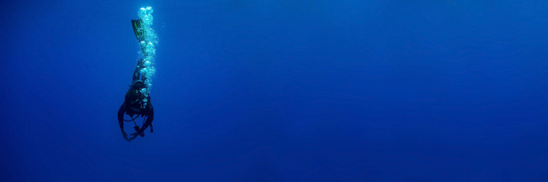 Blue background banner with a scuba diver entering water in a vertical position making bubbles 