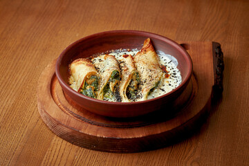 Baked pancakes with chicken and spinach in a creamy sauce on a wooden background. stuffed Crepes or...