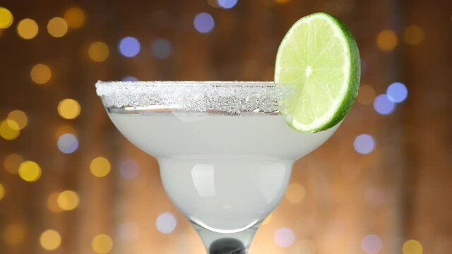 Classic Margarita cocktail over Blinking boken Background, rotate. IBA official cocktail. Party, Success, holiday, celebrating. 4K UHD video
