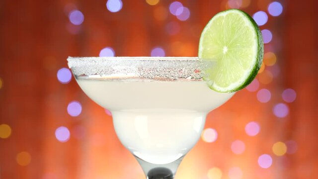 Celebrating with cocktail. Classic Margarita cocktail over Blinking boken Background, rotate.Party, Success, holiday, celebrating. 4K UHD video