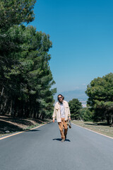 Young man walking down the street with his skateboard in his hand looking at the camera.