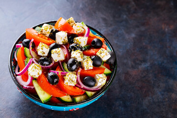 Greek salad in a bowl on a dark background. Healthy salad with feta cheese and olives. Fresh...