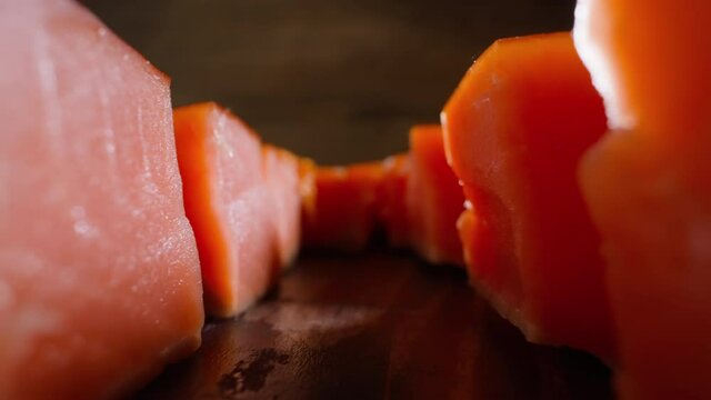 Motion along rows of delicatessen scarlet cool smoked salmon cubes lying on rustic wooden table at bright light extreme closeup slow motion