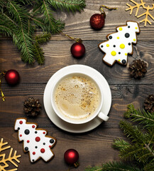 A cup of coffee with delicious milk foam, homemade gingerbread and Christmas decorations on a brown wooden table. The concept of the New Year and Christmas. Christmas card.