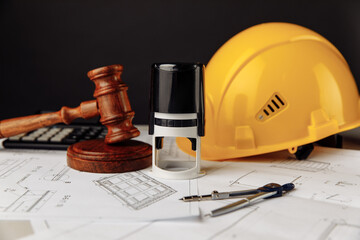 Judge wooden gavel, stamp and yellow helmet with construction plans