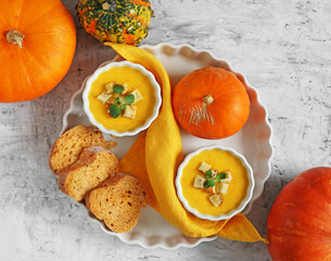pumpkin soup in bowls with slices of bread on the dish and pumpkins nearly, top view