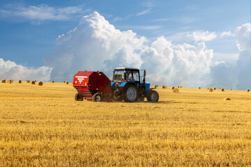 Obraz premium Bales of Hay in the Countryside and Tractor at Work in the background.