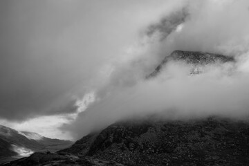 Black and white Epic mountain landscape image of Pen Yr Ole Wen in Snowdonia National Park with low cloud on peak and moodyfeel