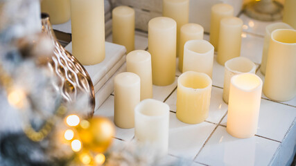 Bright New Year celebration décor. Christmas and New Year interior in light classic style. White room with Xmas Tree decorated, flashing garland, candles and gold balls. Winter Holiday Background