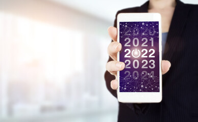 New year concept. Hand hold white smartphone with digital hologram 2022 sign on light blurred background. Happy New Year 2022 -