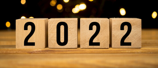 Banner Happy New Year 2022. Wooden blocks with numbers on christmas bokeh background close-up