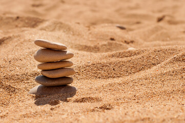 Fototapeta na wymiar Six flat pebbles are stacked on a yellow sandy beach with a place for text on the right side of the frame