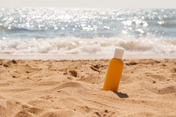 A yellow jar with a white cap with sunscreen stands in the sand on a yellow sandy beach against the background of a blue sea