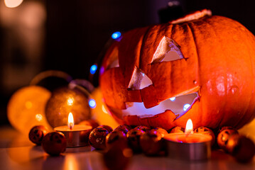Spooky smiling halloween pumpkin in burning fire candles flames. The big helloween symbol has a mad face glowing eyes mouth and glow teeth surrounded by candies.