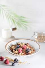 Fototapeta na wymiar Bowl of granola with yogurt, milk and fresh raspberries, blueberries, frozen berries mango for a healthy breakfast on a white marble table 