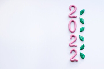 numbers 2022 made of pink plasticine, arranged vertically with space for text on a white background with green plasticine leaves
