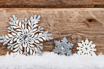 Silvery Christmas snowflakes in the snow on a wooden background.