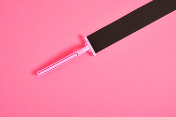 pink plastic disposable razor and black paper triangle on pink background