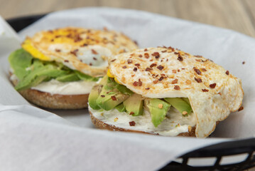 Tasty and hearty breakfast bagel topped with avocado and fried egg sprinkled with pepper flakes