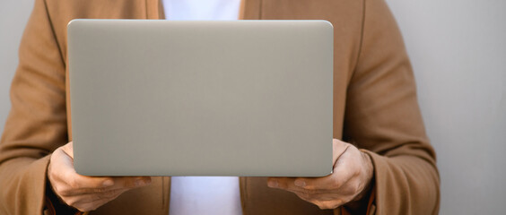Cropped view of laptop in hands of freelancer in coat standing near building , banner 