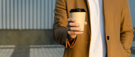 Cropped view of man in brown coat holding coffee to go and hand in pocket outdoors, banner 