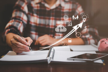 Businessman hand write in book note and icon business graphs with mini wood house model from model on wood table, Planning buy Real Estate, Planning to buy property. concept of Choose the best.